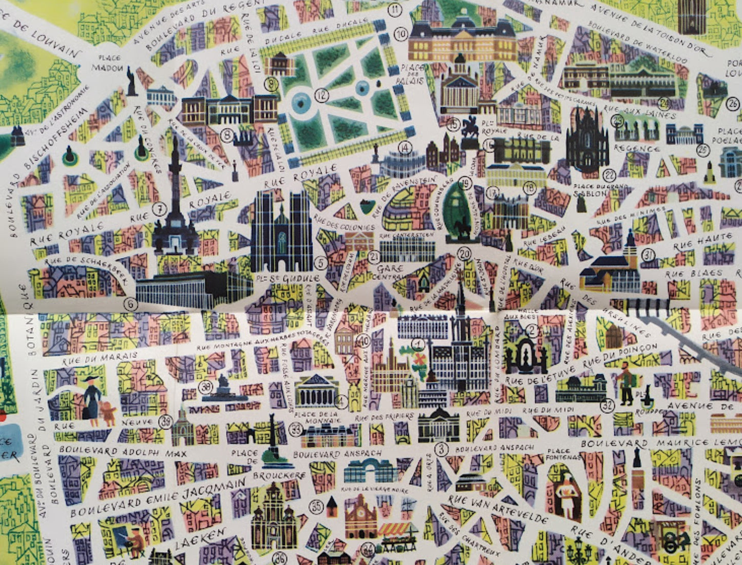 Gros plan sur le centre-ville montrant le tracé des rues et les façades des bâtiments historiques dessinés dans un style artistique avec des touches de rose, bleu et vert.
